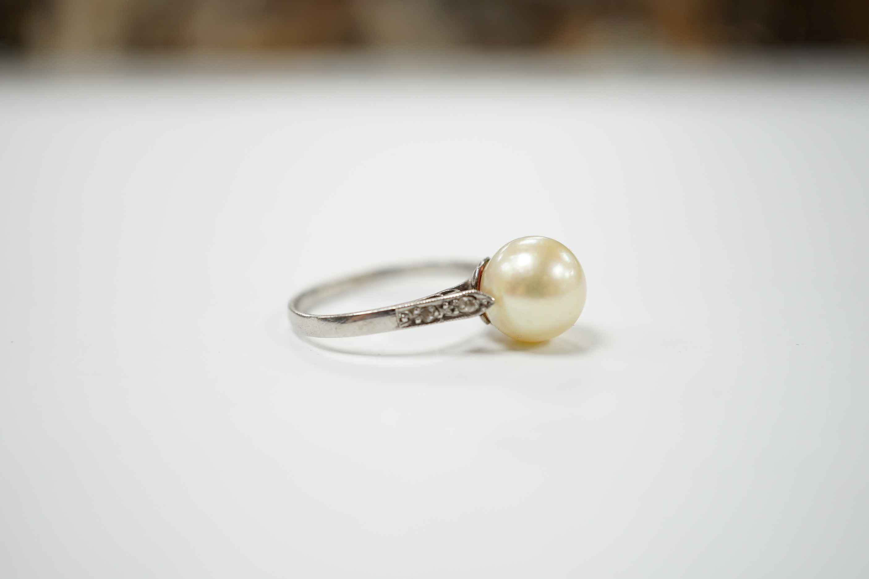 A white metal solitaire cultured pearl ring with diamond set shoulders, size J